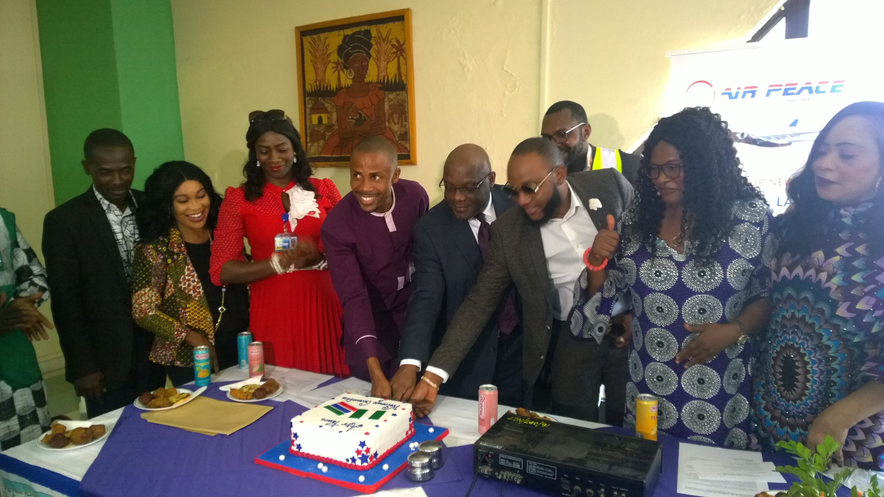 L-R: Air Peace Chief Security Officer, Mr. Monsuru Akinbola, Assistant Customer Relations Manager, Mrs. Patricia Ebilah, Cabin Services Manager, Florence Opia, Corporate Communications Manager, Mr. Chris Iwarah, Nigeria High Commissioner to The Gambia,Ambassador Oluwasegun Ibidapo-Obe, Air Peace Brand Ambassador, Kcee, Deputy Human Resource Manager, Mr. Ume Ume (behind), Airport Coordinator, Mrs. Clementina Ukonze and Revenue Manager, Ihuoma Ukairo cutting the cake to mark the airline’s inaugural flight to Banjul, The Gambia on Monday